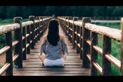 Rear view of woman sitting on wooden railing