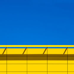 Low angle view of yellow wall against clear blue sky