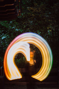 Woman spinning illuminated lightning equipment in forest during night