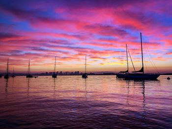 Sailboats in sea against sunset sky