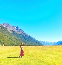 Full length side view of woman walking on land against mountains and clear blue sky during sunny day