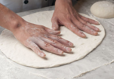 Cropped hands of chef kneading dough on table in commercial kitchen