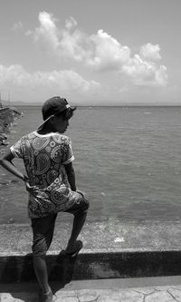 Rear view of teenage boy standing on retaining wall against sea