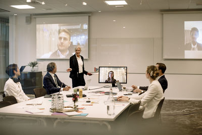 Mature businesswoman giving presentation to colleagues in board room during global conference meeting at office