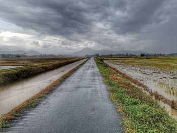 Empty road amidst field against sky during rainy season