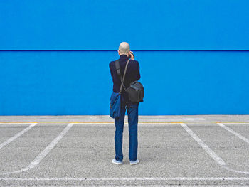 Rear view of man photographing blue wall on road in city