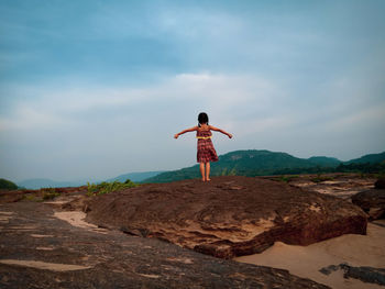 Rear view of man standing on rock against sky