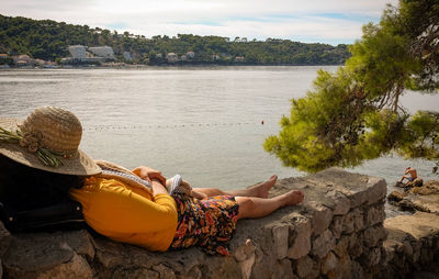 Rear view of woman sitting on rock by lake