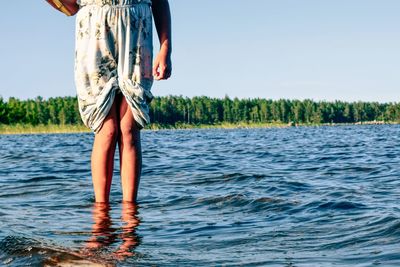 Low section of man standing by lake against sky