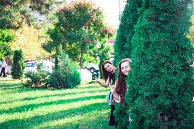 Portrait of friends showing peace sign while hiding behind plants