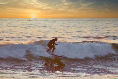 Man surfing in sea against sky during sunset