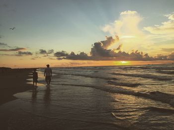 Silhouette man standing on beach against sky during sunset