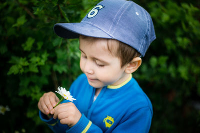 Cute boy holding white flower by plants at park