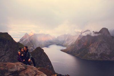 Friends sitting on mountain against sky during foggy weather