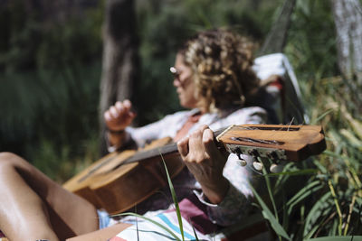 Woman with sunglasses playing guitar lying on a hammock.