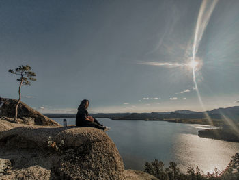 Man sitting on rock by sea against sky