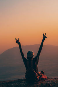 Low angle view of silhouette man with arms raised against mountain and sky during sunset