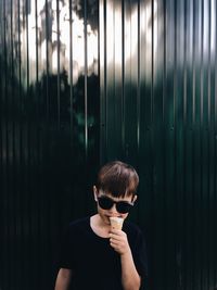 Portrait of boy eating ice cream cone while standing against corrugated iron