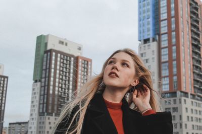 Portrait of beautiful young woman standing against buildings in city