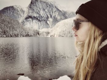 Side view of woman wearing sunglasses while looking away by lake during winter