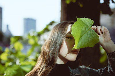 Close-up of smiling young woman covering face with leaf