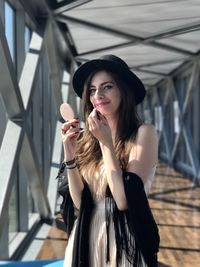 Portrait of young woman applying lipstick at covered walkway