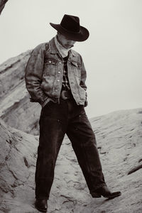 Portrait of young cowboy standing against sky