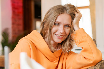 Portrait happy woman in cafe. wearing a bright orange sweatshirt.