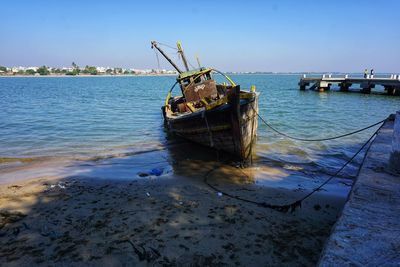 Abandoned boat moored on shore against sky