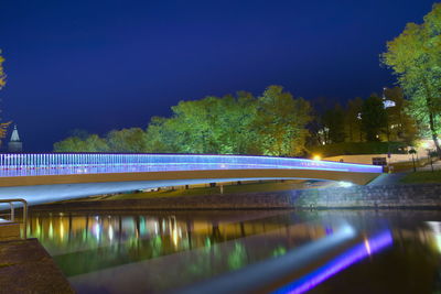 Light trails by bridge against clear blue sky at night