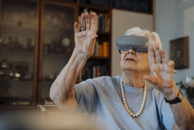 Senior woman wearing virtual reality simulator gesturing at home