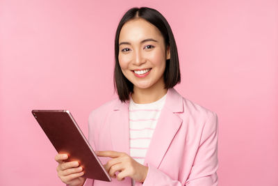 Portrait of young woman using mobile phone while standing against pink background