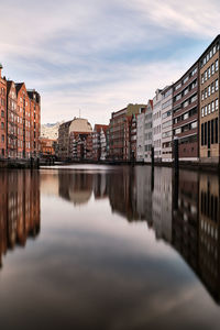 Buildings by river against sky in city