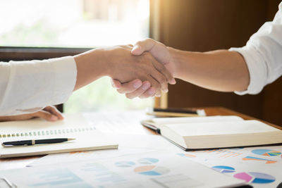 Cropped image of colleagues handshaking above graphs on office desk