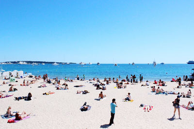 Group of people on beach against clear blue sky