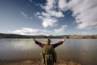 Bushcrafter looking at lake with arms outstretched while standing in nature