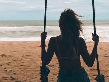 Rear view of woman standing at beach against sky