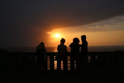 Silhouette people standing at beach during sunset