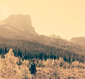 Boy standing on mountain in forest against clear sky