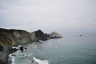 Scenic view of sea by cliff against cloudy sky