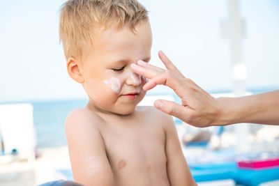 Cropped hand of mother applying suntan lotion on boys face