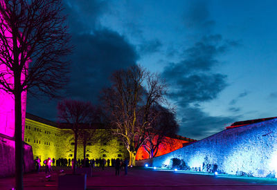 People on illuminated street against blue sky at night