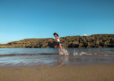 Girl running on beach against clear blue sky