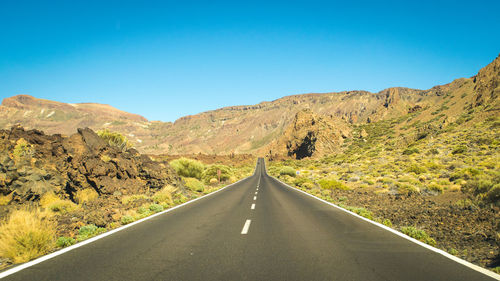 Empty road amidst mountains against clear blue sky