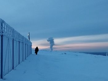 Rear view of person walking on snow covered field against sky