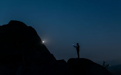 Silhouette man standing on rock against blue sky at night
