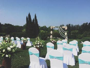 White chairs on grass during wedding reception against clear sky