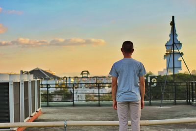 Man standing by railing in city against sky during sunset