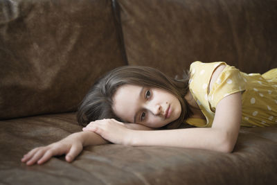 Frustrated thoughtful teen girl lies on the brown couch