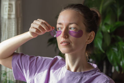 Young woman applying purple hydrogel eye patches against wrinkles, puffiness and dark circles.